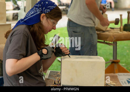 Eine Frau, die beim York Minster Stone Carving Festival, Minster Yard, York, North Yorkshire, England, einen Steinblock mit einem Hammer und Meißel schnitzen konnte. Stockfoto