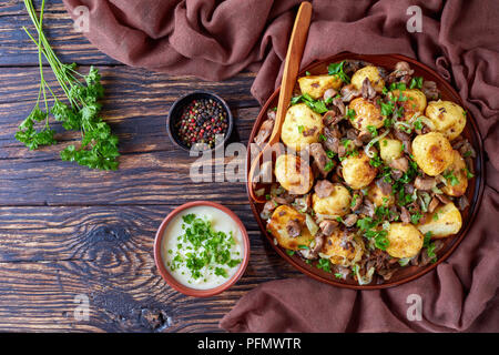 Hausgemachte sauteed neue Kartoffeln mit wilden Steinpilzen, Zwiebeln und Gewürze auf einem Teller mit Löffel aus Holz auf einem alten rustikalen Tisch mit Sahnesauce, Clo Stockfoto