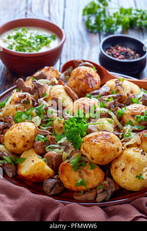 Nahaufnahme der hausgemachten sauteed neue Kartoffeln mit wilden Steinpilzen, Zwiebeln und Gewürze auf einem Teller mit Löffel aus Holz auf einem alten rustikalen Tisch mit Sahne Stockfoto