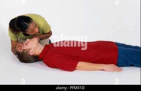 Frau kniete über den Menschen liegen auf dem Boden, seine Atmung prüfen Stockfoto