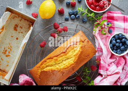 Frisch gebackene Zitronenkuchen oder Pound Cake mit Beeren füllen auch bekannt als Torte de voyage Kuchen auf einer konkreten Tabelle mit Beeren und Zitrone, Französisch cui Stockfoto