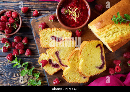 In der Nähe von frisch gebackenen aufgeschnittene Zitrone Pound Cake mit himbeermarmelade füllen auch als Torte de voyage Kuchen auf einem alten Holztisch bekannt, dunklen rustikalen s Stockfoto