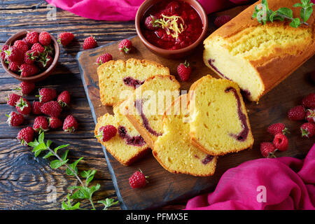 Nahaufnahme der Zitrone Pound Cake mit himbeermarmelade Füllen auf einem Schneidebrett einer alten dunklen Holztisch mit frischen Beeren, rustikaler Stil, französische Küche, Stockfoto