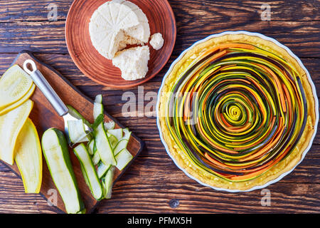 Pflanzliche Spirale Quiche mit Zucchini, Aubergine, Möhren Schichten mit Ricotta Füllung in einer Auflaufform auf einem alten rustikalen Tisch mit Zutaten, v Stockfoto