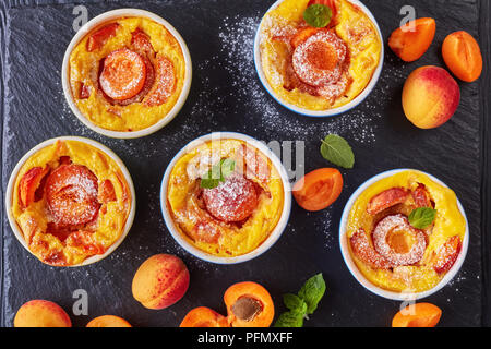 Köstliche französische Sommer dessert Gebackene Aprikosen clafoutis in Förmchen auf schwarzem Schiefer Fach, auf einem Holztisch, Ansicht von oben, flach, close-up Stockfoto