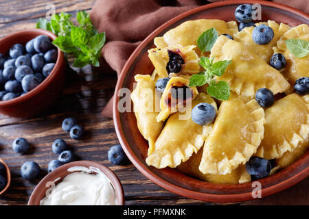 Süße Knödel, Pierogi, vareniki mit blaubeere Füllungen in einem Ton Schüssel auf einem dunklen rustikalen Tisch mit saurer Sahne und frischen Beeren, horizontale Ansicht fr Stockfoto