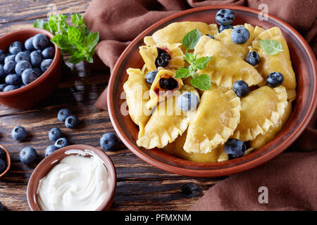 Süße Knödel, Pierogi, vareniki mit blaubeere Füllungen in einem Ton Schüssel auf einem dunklen rustikalen Tisch mit saurer Sahne und frischen Beeren, horizontale Ansicht fr Stockfoto