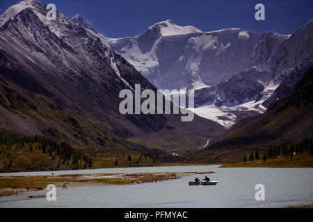 Ein Schiff mit Touristen kreuzt ein See umgeben von schneebedeckten verhangene Berge des Altai, in Russland, in der Nähe der Grenze zu Kasachstan Stockfoto