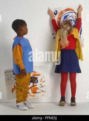 Mädchen, dass Gemälde an der Wand, Junge neben ihr zusehen und ein anderes Gemälde in seiner Hand Stockfoto