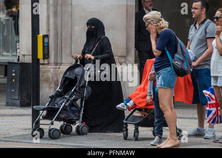 London, Großbritannien. 22 August, 2018. Eine muslimische Frauen in einem Kopftuch und Burka schiebt einen Kinderwagen in der Oxford Street - ein normaler Anblick in der gemischtes Publikum einkaufen. Credit: Guy Bell/Alamy leben Nachrichten Stockfoto