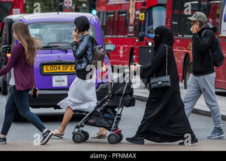 London, Großbritannien. 22 August, 2018. Eine muslimische Frauen in einem Kopftuch und Burka schiebt einen Kinderwagen in der Oxford Street - ein normaler Anblick in der gemischtes Publikum einkaufen. Credit: Guy Bell/Alamy leben Nachrichten Stockfoto