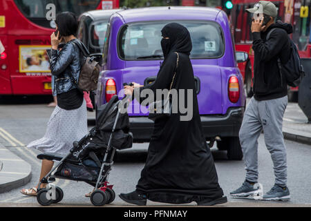 London, Großbritannien. 22 August, 2018. Eine muslimische Frauen in einem Kopftuch und Burka schiebt einen Kinderwagen in der Oxford Street - ein normaler Anblick in der gemischtes Publikum einkaufen. Credit: Guy Bell/Alamy leben Nachrichten Stockfoto