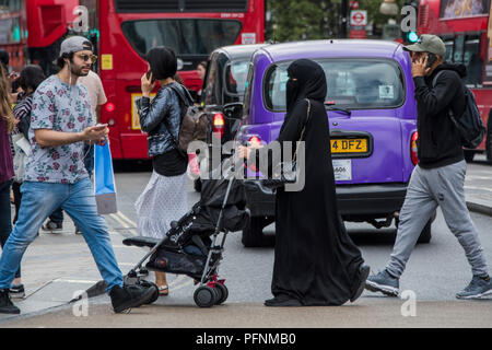 London, Großbritannien. 22 August, 2018. Eine muslimische Frauen in einem Kopftuch und Burka schiebt einen Kinderwagen in der Oxford Street - ein normaler Anblick in der gemischtes Publikum einkaufen. Credit: Guy Bell/Alamy leben Nachrichten Stockfoto