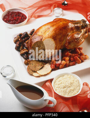 Weihnachten Truthahn serviert mit gewalzten durchwachsener Speck Speckscheiben und Chipolatas, Abschnitt der Türkei in Scheiben weg offenbart Anfüllen und gekochtes Putenfleisch. Krug mit Soße, Brot, Soße und Cranberry Sauce separat. Stockfoto