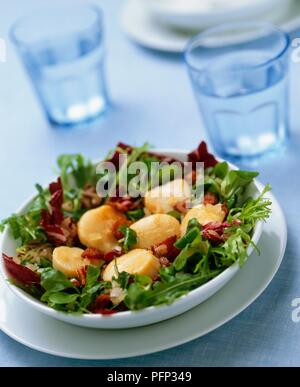Warmer Kartoffelsalat mit gebratenen Speck serviert in einer Schüssel, Gläser Wasser im Hintergrund Stockfoto