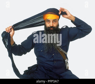 Mann einwickeln Dunkelblau Turban um den Kopf über eine Orange base Turban Stockfoto