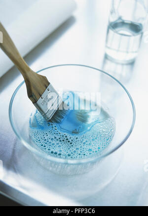 Pinsel, mit der blauen Farbe auf Borsten, Einweichen in Glas Schüssel mit lauwarmem Wasser und einer kleinen Menge der Sanften Chemie Spülmittel Stockfoto