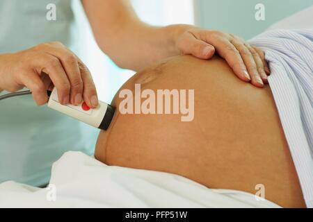 Die Hebamme überwacht babys Herzschlag mit Handbediengerät, während der ersten Phasen der Arbeit, close-up Stockfoto