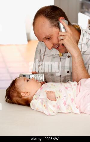 Mann mit Handy am Ohr und ein anderes Mobiltelefon am Ohr des Babys Stockfoto