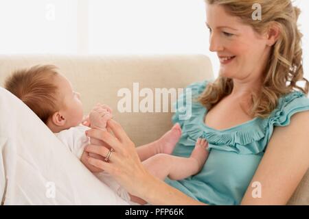 Frau sitzt auf einem Sofa mit Blick auf Baby Mädchen lächelnd Stockfoto