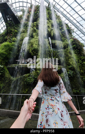 Porträt der schönen Asiatin führt Ihr Partner mit der Hand, um den Wasserfall von Cloud Forrest. Cloud Forrest ist ein Wintergarten Kuppel bei GBTB. Stockfoto