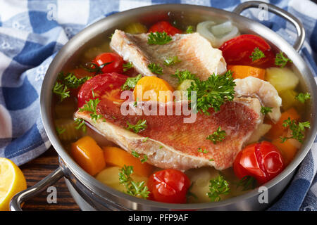 Herzhafte Fischsuppe - Griechische psarosoupa in eine Kasserolle auf einem alten Holz- rustikalen Tisch mit Küchentuch, Nahaufnahme, Seite, Ansicht von oben Stockfoto