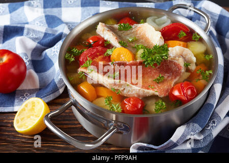 Herzhafte Fischsuppe - griechische Küche psarosoupa in eine Kasserolle auf einem alten Holz- rustikalen Tisch mit Küchentuch und die Hälfte eines aus gepressten Zitrone, Cl Stockfoto