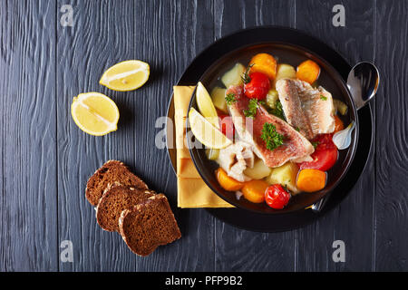 Herzhafte Fischsuppe - Griechische psarosoupa serviert in einem schwarzen Schüssel auf einen Holztisch mit Serviette und Löffel, Ansicht von oben, flach Stockfoto