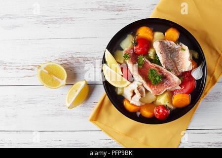 Herzhafte Fischsuppe - Griechische psarosoupa mit Zitronenscheiben in einer schwarzen Schüssel serviert auf einem weißen Holztisch mit Serviette, Ansicht von oben Stockfoto