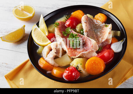 Herzhafte Fischsuppe - Griechische psarosoupa mit Zitronenscheiben in einer schwarzen Schüssel serviert auf einem weißen Holztisch mit Serviette, Ansicht von oben, close-up Stockfoto