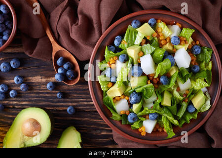 Mexikanischer Salat mit Blaubeeren, römersalat Blätter, jicama, gebraten knusprige Maiskerne und Avocado auf einer Platte auf einem alten rustikalen Holztisch mit Stockfoto