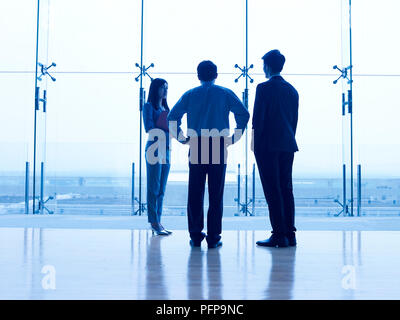 Die Silhouetten der drei asiatischen Führungskräfte stehen vor Fenster diskutieren. Stockfoto