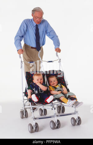 Mann mit grauen Haaren treibt ein doppeltes Kinderwagen mit zwei Kleinkinder in Stockfoto
