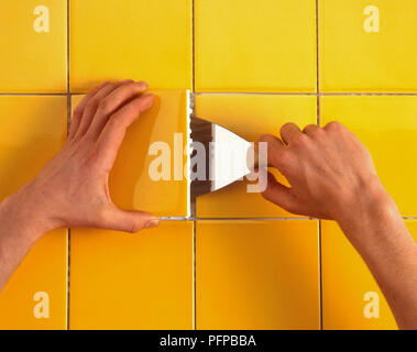 Hand Kelle gelb Keramik aus Bad Wand zu entfernen, close-up Stockfoto