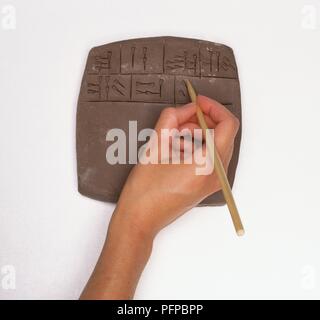 Hand mit einem spitzen Reed zu schreiben Keilschrift auf Platte aus Ton, close-up Stockfoto