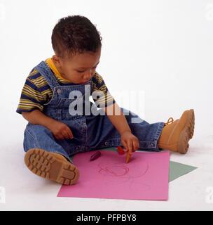 Junge sitzen in Jeans latzhose Zeichnung auf Papier mit Buntstiften Stockfoto