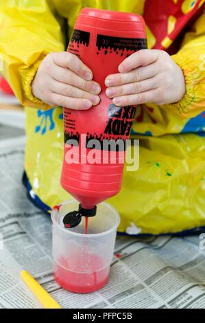 Child's Hände quetschen Rohr mit roter Farbe in den Topf Stockfoto