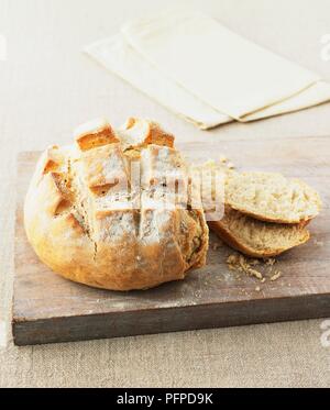 Sauerteigbrot Laib auf Holz gehackt Board mit zwei Scheiben und Servietten im Hintergrund Stockfoto