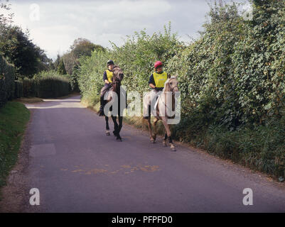 Zwei junge Frauen mit Leuchtstoff tops reiten Ponys auf Feldweg Stockfoto