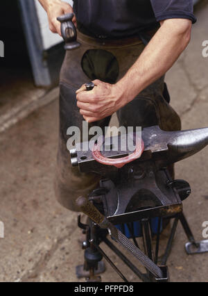 Schmied, Bohrungen in geschmolzenem Hufeisen auf Amboss, close-up Stockfoto