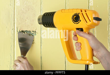 Mit einer Heißluftpistole und Abstreifer Farbe von einer hölzernen Oberfläche zu streifen Stockfoto