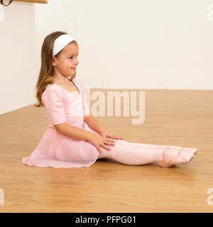 Mädchen in Ballerina Outfit sitzen auf dem Boden und nach Zehen, 5 Jahre alt Stockfoto