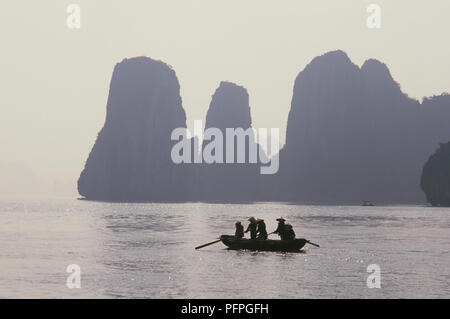 Vietnam, Bai Tu Long Bay, Silhouette der Menschen im Ruderboot, Van Don Insel Felsen im Hintergrund Stockfoto