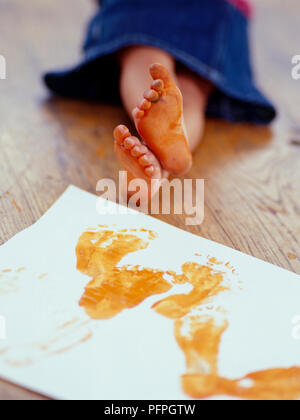 Orange Farbe auf fußsohlen Girl's Füße neben Papier mit Fußabdrücke auf Holzboden Stockfoto