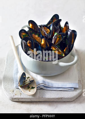 Moules marinieres diente in Schüssel auf Schneidebrett mit Holzlöffel Stockfoto