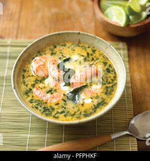 Keralan Crevetten Suppe Überbacken mit Curry Blätter in der Schüssel serviert auf Unterlage mit Löffel und in Scheiben geschnittenen Limetten, close-up Stockfoto