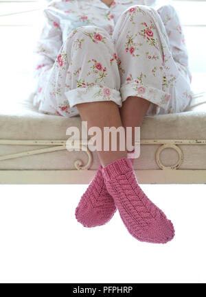 Frau sitzt auf dem Bett tragen Schlafanzug und Rosa gestrickten Socken Stockfoto