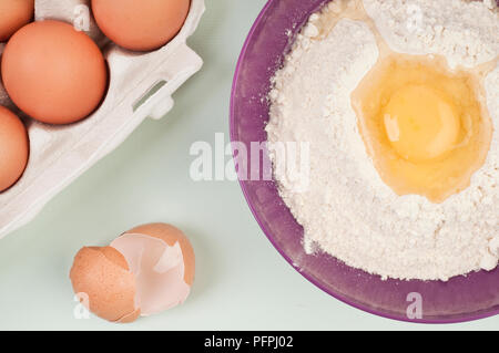 Backzutaten einschließlich Karton Eier, Ei und Mehl in Schüssel, und zerbrochene Eierschale, Ansicht von oben, close-up Stockfoto