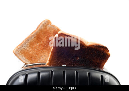 Zwei Scheiben geröstetes Weißbrot, eine Scheibe ist verbrannt, im Toaster auf weißem Hintergrund, Nahaufnahme Stockfoto