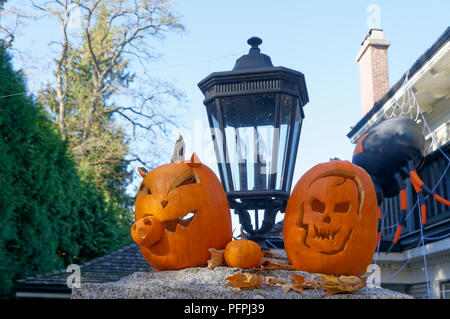 Zwei geschnitzte Halloween Kürbisse oder Jack-o'-lanterns auf einer Steinmauer vor einem Haus Stockfoto